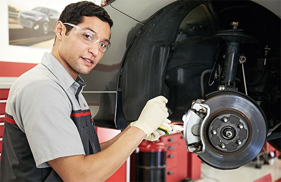 Service Tech looking at camera next to a brake pad / rotor